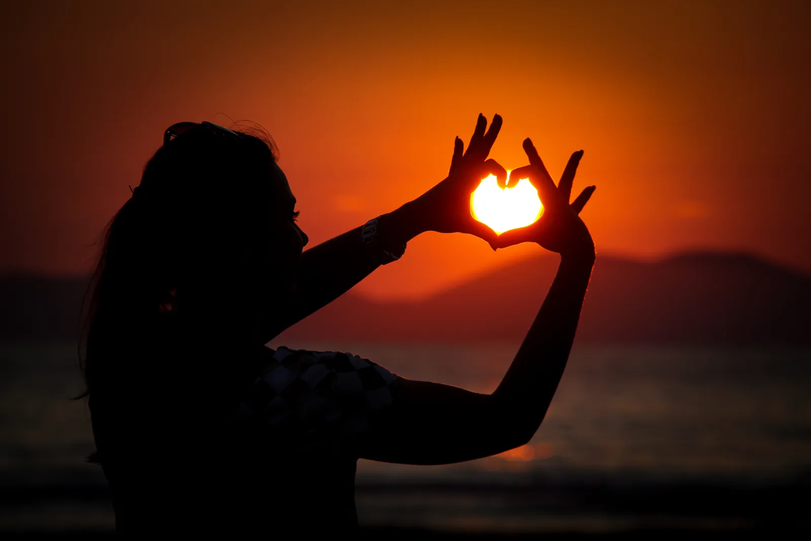 Silhouette einer Frau, die mit den Händen ein Herz um die Sonne formt